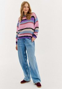 Pletený svetr v pruhovaných odstínech růžové, modré a fialové, v kombinaci s širokými modrými džíny a burgundskými botami. Měkká textura a uvolněný střih.
