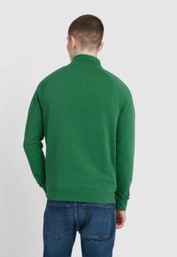 Green sweatshirt with a high collar, long sleeves, and ribbed cuffs; paired with blue denim jeans. Smooth texture, casual fit.
