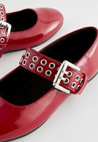 Rote Lackleder-Mary-Jane-Ballerinas mit runden Zehen, ausgestattet mit einem breiten Riemen mit silbernen Ösen und einer metallischen Schnalle.
