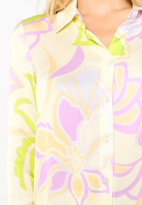 Košile s dlouhým rukávem, světle žlutého základu, s velkými pastelovými květinovými vzory v růžových, zelených a béžových tónech.