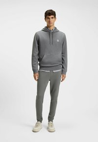 Gray hooded sweatshirt with front pocket and logo, paired with slim-fit gray pants and light-colored sneakers. Smooth fabric texture.