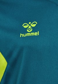 Tissu sarcelle avec logo hummel vert citron présentant une abeille stylisée au-dessus du nom de la marque en minuscules sur des vêtements de sport.