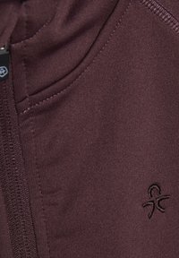 Bordeaux zip-up jacka med en slät yta, med en logotyp på bröstet och detaljerad sömnad längs kanterna.