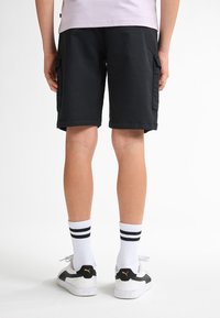 Sorte cargo shorts med sidelommer, opsmøget kant og en afslappet pasform, parret med hvide sokker med sorte striber og sorte og hvide sneakers.
