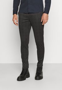 Pantalon à carreaux noirs coupe slim, confectionné dans un tissu texturé, associé à des bottes de combat noires, offrant une finition élégante.