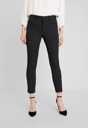 Pantalones negros con un diseño ajustado, que presentan formas blancas en forma de diamante. El material parece suave y tiene una longitud hasta el tobillo. Estilizados con tacones negros.