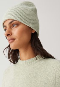 Light green ribbed knit beanie with a soft texture, worn with a matching light green sweater featuring a round neckline and ribbed cuffs.