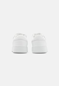 Baskets blanches avec un dessus en cuir lisse, bout arrondi, col rembourré et semelle en caoutchouc texturée, présentant des coutures minimales et un design à lacets.