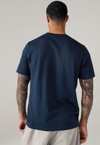 Marineblauwe katoenen t-shirt met korte mouwen, voorzien van een gestructureerd gestreept patroon op de achterkant. Ontworpen met een ronde hals.
