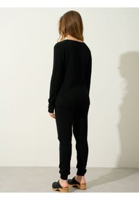 Suéter negro de punto y joggers a juego, con un corte holgado y mangas largas. El modelo lleva unos zuecos negros con suelas de madera.