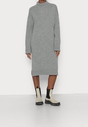 Robe tricotée grise longueur genou avec manches longues et col montant, associée à des bottines beige et noir à semelle épaisse.