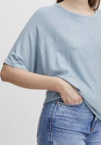 Lyseblå, løst siddende strikket top med vid halsudskæring og korte ærmer, kombineret med højtaljede, falmede blå denimjeans.