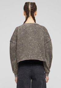 Kuttet, oversized hettegenser i dempet grågrønn, med en teksturert overflate og ribbestrikket halslinning. Kombinert med høyt liv mørke jeans.
