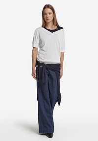 Maglione bianco a maniche corte con colletto blu navy sovrapposto a un top blu navy, abbinato a pantaloni di denim blu scuro larghi e cintura blu navy annodata.