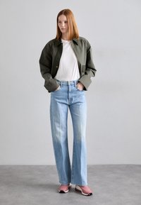 Jachetă verde, tricou alb, blugi largi de un albastru deschis și pantofi sport roz. Texturi netede cu accente de culoare contrastante.