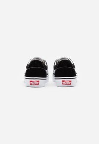 Schwarze Wildledersneaker mit weißen Gummisohlen. Sie verfügen über ein auffälliges rotes Logo an der Ferse und kontrastierende weiße Nähte entlang der Kanten.