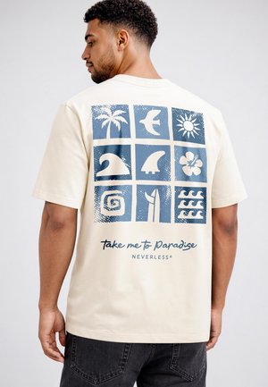 Man wearing a cream t-shirt with blue tropical icons and the text "Take me to Paradise" on the back, standing against a plain background.