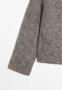 Wool-blend grey coat sleeve with a smooth texture, clean lines, and a side pocket. Features stitching along the cuff and seam details.