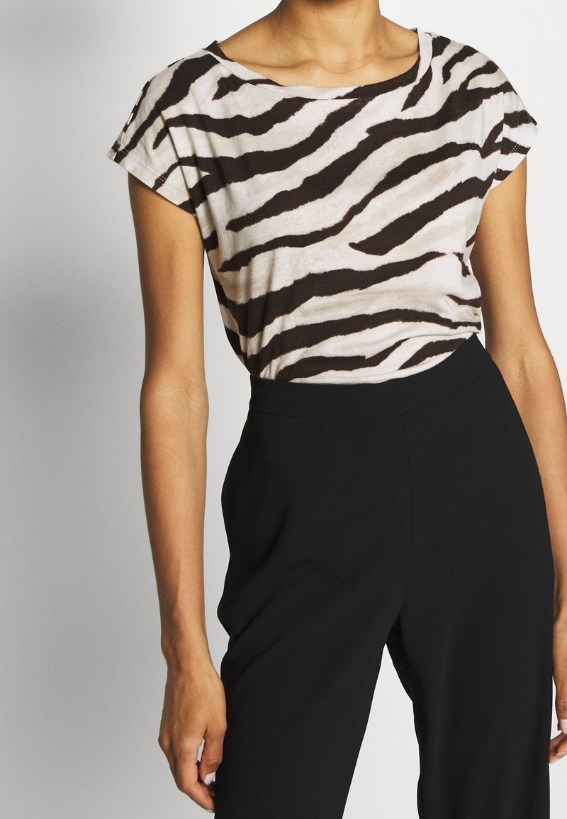 Kvinna som bär en kortärmad zebra-mönstrad topp instoppad i högmidjade svarta byxor, visad från nacke till höfter mot en enkel bakgrund.