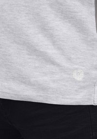 Sweat-shirt gris clair en tissu doux et texturé ; présente un petit logo blanc sur le bas et un design simple et minimaliste.