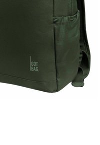 Zaino in tessuto verde con superficie testurizzata, dotato di una tasca laterale e un logo stampato di un verde chiaro. Cinghia regolabile e dettagli della cucitura resistenti.