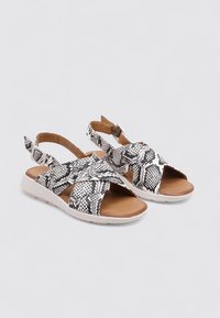 Sandales en imprimé serpent noir et blanc avec des sangles croisées, une semelle intérieure marron et une semelle en caoutchouc blanche ; sangle de cheville réglable incluse.
