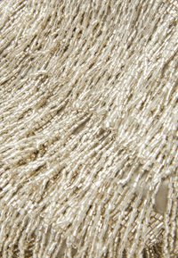 Gros plan sur de petites perles cylindriques translucides et argentées, densément emballées et disposées en brins ondulés.