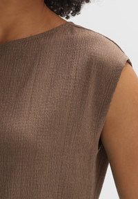 Brun, strukturerad ärmlös topp med rund halsringning. Lättviktigt tyg med en subtil vågeffekt som ger ett mjukt utseende.