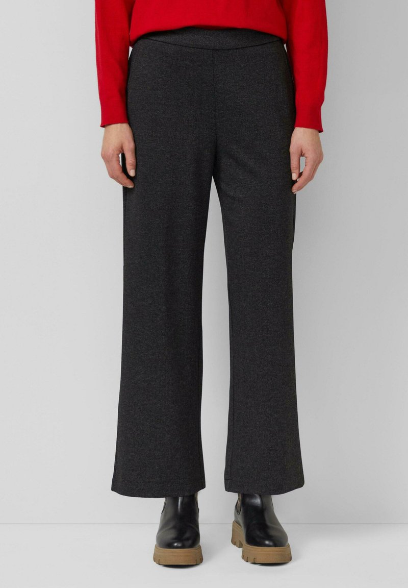 Dunkelgraue, weite Hosen aus weichem Stoff mit hoher Taille und ohne sichtbare Verschlüsse. Kombiniert mit schwarzen Stiefeletten.