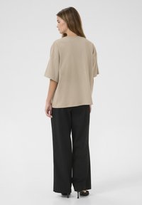 Beige oversized t-shirt met korte mouwen, gladde textuur, gecombineerd met brede zwarte broek, met een rechte snit en subtiele glans.