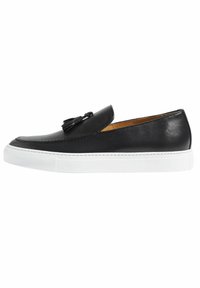 Scarpa slip-on in pelle nera con suola in gomma bianca, dotata di un nastro decorativo e cuciture dettagliate lungo il bordo. Texture liscia.