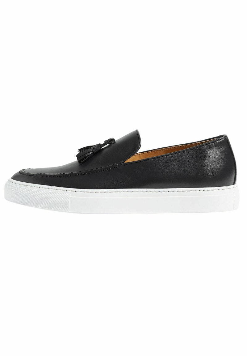 Scarpa slip-on in pelle nera con suola in gomma bianca, dotata di un nastro decorativo e cuciture dettagliate lungo il bordo. Texture liscia.