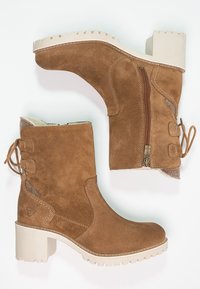 Bottes chelsea en daim marron avec des talons épais beiges, fermeture éclair sur le côté, détails cousus et lacets à l'arrière, présentées en vues latérales et de la semelle.