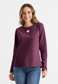 Bordeaux langemouwen shirt met een ronde hals, voorzien van een klein wit hartdetail op de borst en een label op de linkermouw.