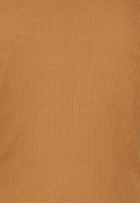 Ribbestrikket topp i en varm, dempet oransjefarge, med en myk tekstur og vertikale linjer. Stoffet ser strammende og formtilpasset ut.