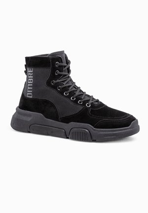 Zapatilla negra de caña alta con suela gruesa, cordones en la parte delantera, paneles de ante y tela, y la palabra "OMBRE" impresa en el lateral.