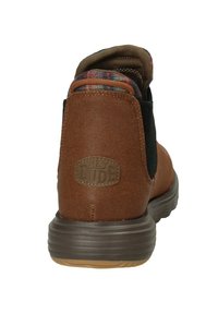 Botte de cheville en toile marron avec une tige texturée, des accents noirs et une doublure en plaid. Dotée d'une semelle en caoutchouc avec un patch de marque sur le talon.