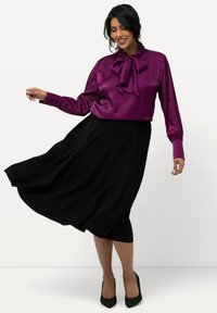 Paarse satijnen blouse met een strikdetail, gecombineerd met een zwarte, vloeiende rok. De hakken zijn puntig en hebben een gestructureerde afwerking.