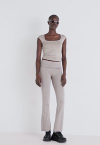 Beige fitted top with a square neckline, paired with beige flared pants. Model wears black chunky sneakers and light-colored sunglasses.