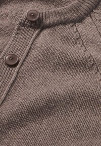 Ruskea neulepusero, jossa on ribbireunus ja kaksi pyöreää ruskeaa nappia edessä, esittelee tekstuurista, pehmeää kangaspintaa.