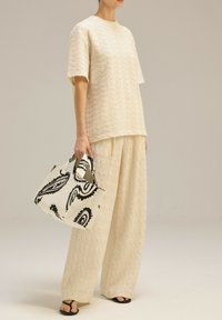 Beżowa, teksturowana bluzka i szerokie spodnie, w połączeniu z białą torbą z czarnym wzorem paisley. Całość uzupełniają czarne klapki.