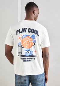 Valge puuvillane T-särk, millel on multika stiilis korvpallitegelane, tekst "PLAY COOL" ja rulluiskude graafika. Lühikesed varrukad, mugav lõige.