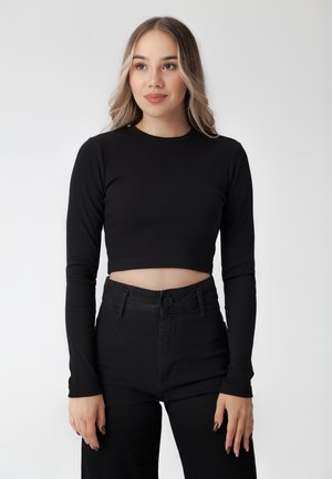 Top corto a maniche lunghe nero a coste con scollatura rotonda abbinato a pantaloni in denim neri a vita alta con chiusura frontale a bottoni.