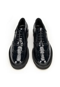 Černé lakované boty s wingtip designem, doplněné o brogue detaily, se šesti otvory pro šněrování a silnou černou gumovou podrážkou.