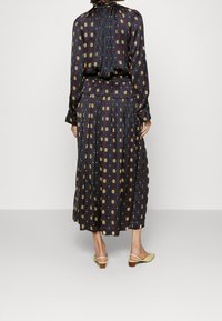 Musta pitkähihaisessa mekossa on monivärinen geometrinen kuosi, kerätty vyötärö ja laskostettu hame; yhdistettynä keltaisiin liukuviin korkokenkiin.