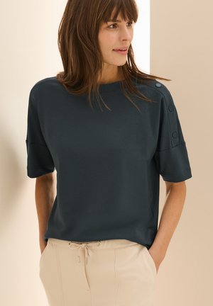 T-shirt manches courtes bleu foncé avec une coupe ample, présentant des accents de boutons sur les épaules. Tissu lisse et design col ras du cou.