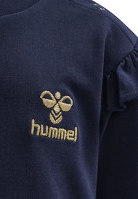 Navyblå bomullsblus med volangärmdetalj och guldbroderad bi-logotyp med "hummel" text nedanför på vänster bröstficka.