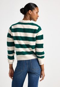 Grøn- og cremefarvet stribet sweater med ribbet krave og mansjetter, lavet af blødt materiale, båret over højtaljede blå jeans.