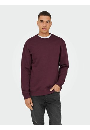 Bordeaux sweatshirt van zachte stof, met een ronde halslijn, ribgebreide mouwen en onderkant, gedragen over een wit t-shirt, gecombineerd met donkere jeans.