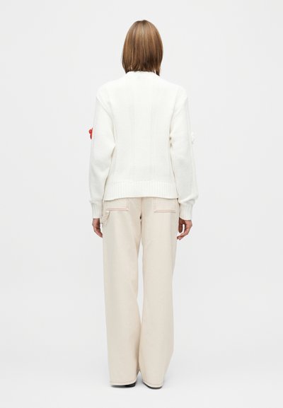 Hvit strikket genser med ribbestrikkede mansjetter og nederkant, kombinert med løstsittende beige bukser med lyse sømdetaljer.